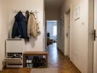 Hol îngust de bloc cu pantofar puțin adânc, cârlige și banchetă pe o latură, peretele opus liber și parchet continuat din living